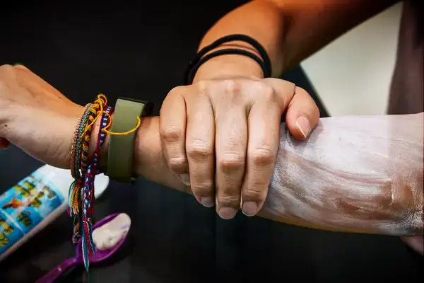 A hand spreading Maui Surfer Honey All Natural Sunscreen across an arm against a dark background