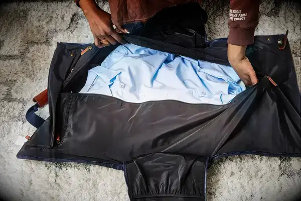 Hands zipping the Mark & Graham Commuter 2-in-1 Garment Bag with clothing inside
