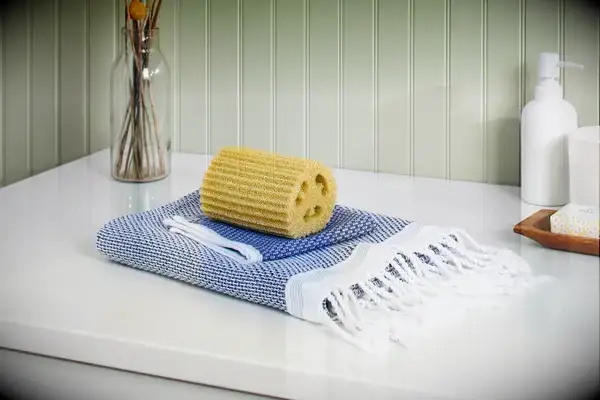 Folded Coyuchi Mediterranean Organic Towel and washcloth with a sponge on a bathroom counter