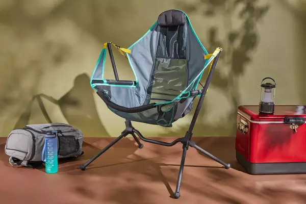 NEMO Moonlite Reclining Camp Chair on a brown floor next to a backpack and a cooler