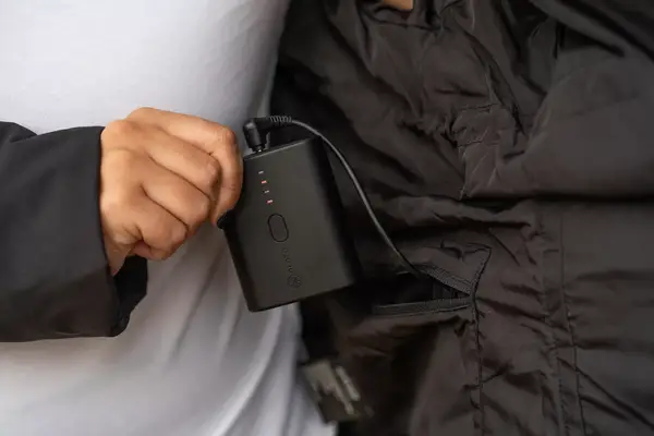 A hand holding the battery pack attached to the pocket of the ORORO SOHO Women