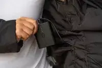A hand holding the battery pack attached to the pocket of the ORORO SOHO Women