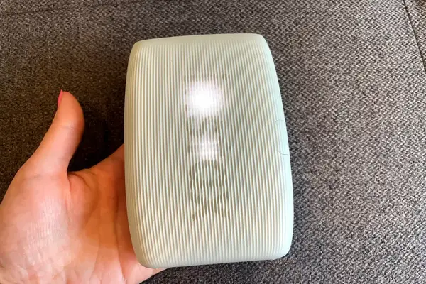 A person holding a grooved rectangular object with text partially visible on its surface placed against a textured background