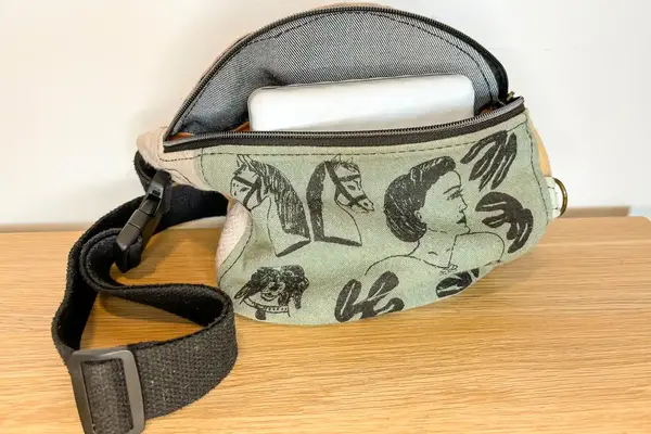 A fabric belt bag with illustrated designs featuring faces horses and hands containing an object partially visible inside