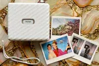 Instax printer device alongside colorful instant photograph prints on a decorative background