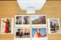 Polaroid photos arranged on a table under a Fujifilm Instax device featuring various people and scenes