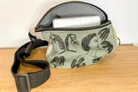A fabric belt bag with illustrated designs featuring faces horses and hands containing an object partially visible inside