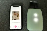 A smartphone displaying an edited photo of a couple with a dog alongside a Fujifilm Instax mini printer
