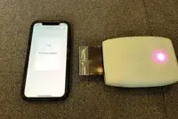 A smartphone displaying Printing in progress next to a Fujifilm Instax photo printer outputting an image