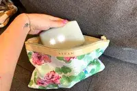 A hand holding an object above a pouch with floral patterns seated on a sofa