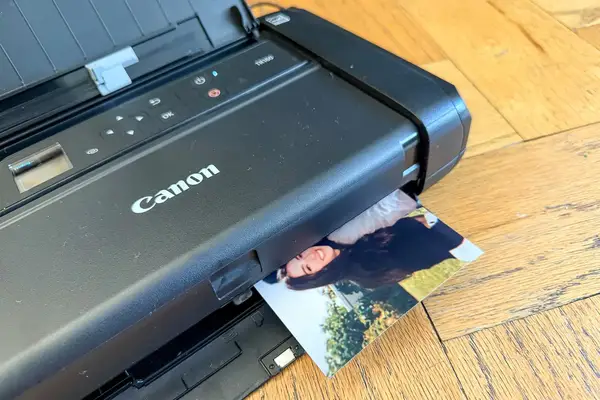 A Canon printer printing a photo of a smiling person on a wooden surface
