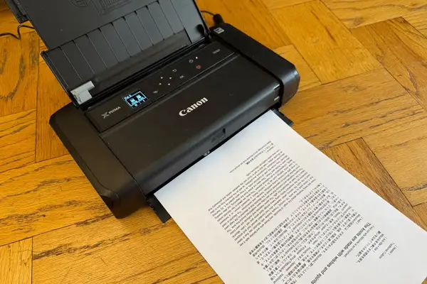 Canon PIXMA printer with a document being printed situated on a wooden floor