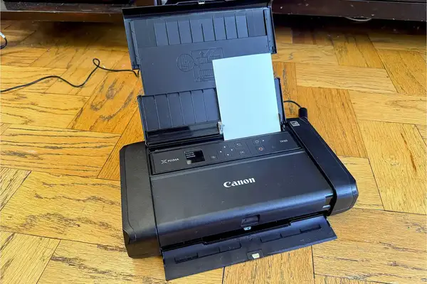 A Canon Pixma TR150 portable printer with the lid open and paper loaded