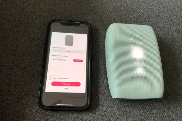 A smartphone displaying a printer connection interface next to a compact portable printer