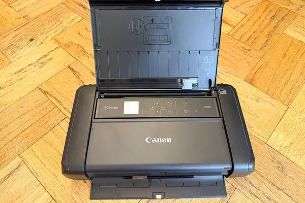 Compact Canon Pixma TR160 printer with open paper feed tray on a wooden floor