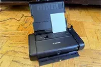 A Canon Pixma TR150 portable printer with the lid open and paper loaded