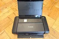 Compact Canon Pixma TR160 printer with open paper feed tray on a wooden floor