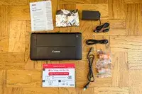 Components of a Canon printer including the device power adapter cables ink cartridges and setup instructions