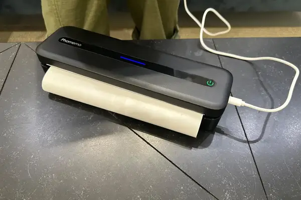 Compact thermal printer with paper loaded power indicator illuminated placed on a textured surface with a connected cable