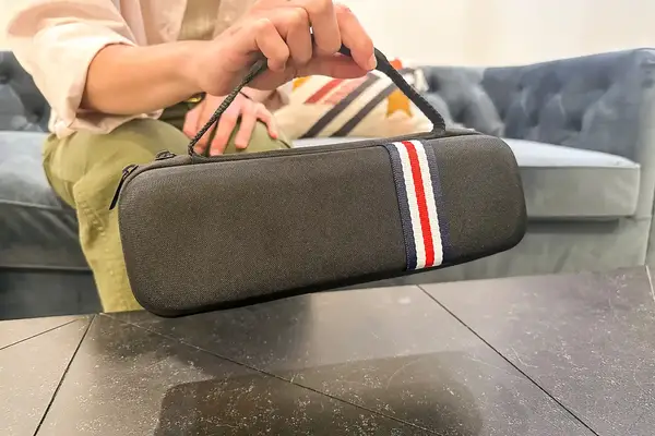 A hand holding a small rectangular black carrying case with a handle and a striped design