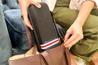 A person places a black pouch with a striped pattern into a brown bag