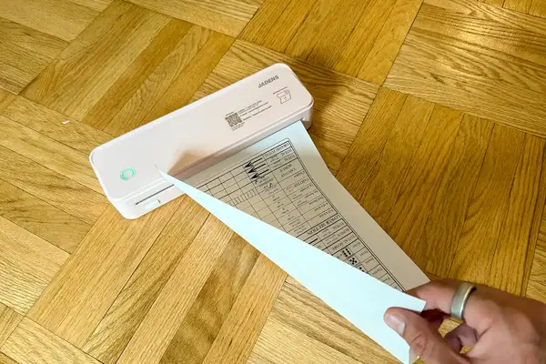A person using JADENS Bluetooth Thermal Printer to print a form on a wooden floor