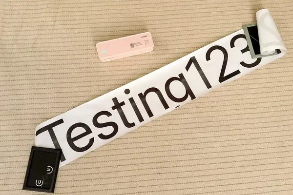 JADENS Bluetooth Thermal Printer with a sample printout saying Testing123 placed on a textured surface