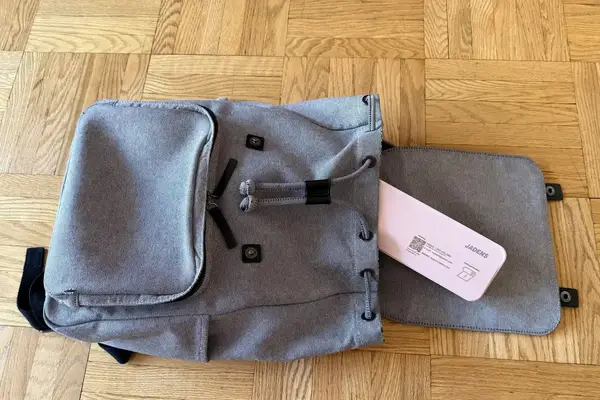 A backpack with its front pocket open revealing JADENS Bluetooth Thermal Printer on a wooden floor
