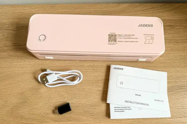 JADENS Bluetooth Thermal Printer with accompanying items including a USB cable an adapter and a user manual on a wooden surface