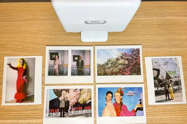 Polaroid photos arranged on a table under a Fujifilm Instax device featuring various people and scenes