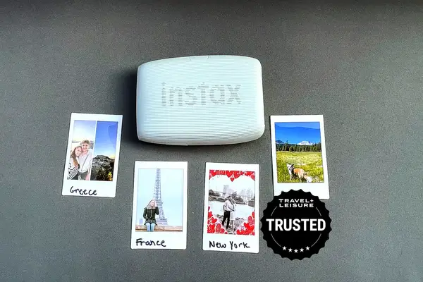 A portable Instax printer displayed with four printed mini photos labeled Greece France New York and a nature scene and a Travel Lanetrek Trusted badge