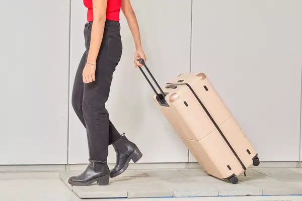 Person rolling the July Checked Plus Large Luggage over pavers