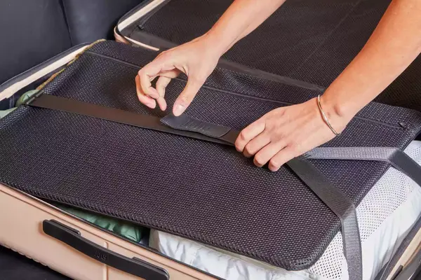 Hands strapping down clothing in the July Checked Plus Large Luggage