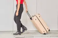 Person rolling the July Checked Plus Large Luggage over pavers