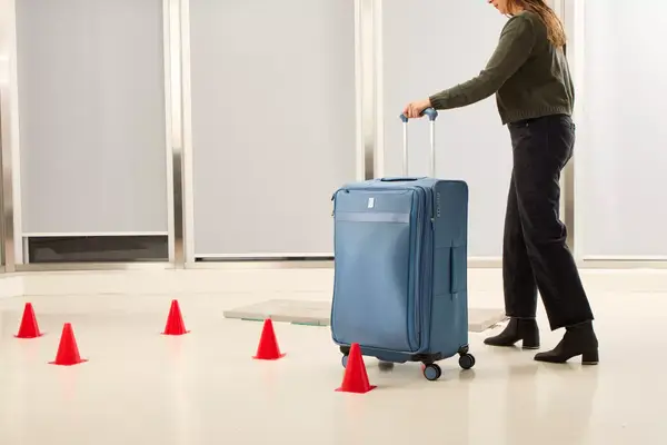 A person wheels the Travelpro VersaPack+ Large Check-In over a floor