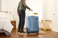 A person wheels the Travelpro VersaPack+ Large Check-In over a rug