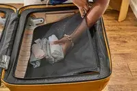 A person places clothing into the mesh pocket inside the Samsonite Proxis Medium Spinner