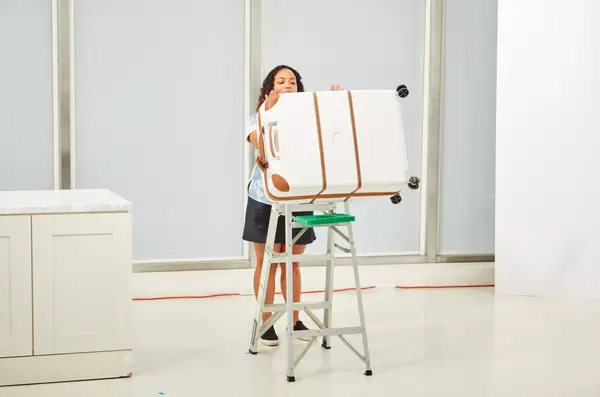 A person pushing the Delsey Paris Chatelet Air 2.0 28 Inch Large Checked Spinner off of a ladder