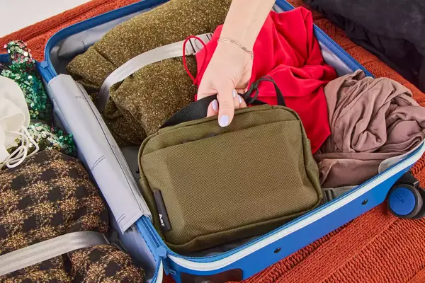A person places the Aer Travel Kit 2 into a packed suitcase