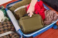 A person places the Aer Travel Kit 2 into a packed suitcase