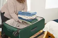 A person places a folded stack of clothes into the Antler Soft Stripe Lightest Large Luggage