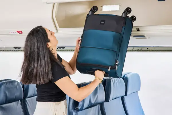 A person places the Antler Soft Stripe Carry-On into an overhead compartment