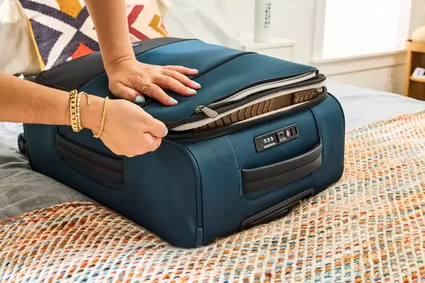 A person zips a pocket on the Antler Soft Stripe Carry-On closed
