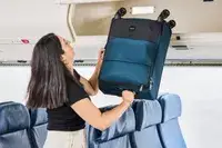 A person places the Antler Soft Stripe Carry-On into an overhead compartment