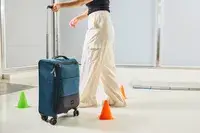A person rolls the Antler Soft Stripe Carry-On around cones