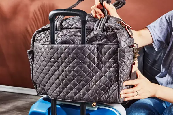 Person placing the MZ Wallace Nik Duffel over a luggage handle