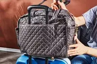 Person placing the MZ Wallace Nik Duffel over a luggage handle