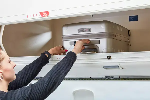 A person placing the Arlo Skye Zipper Carry-on Max into an overhead bin on an airplane