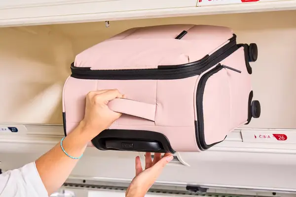 A person putting the Calpak Luka Soft-sided Mini Carry-on Luggage in an overhead compartment of a plane