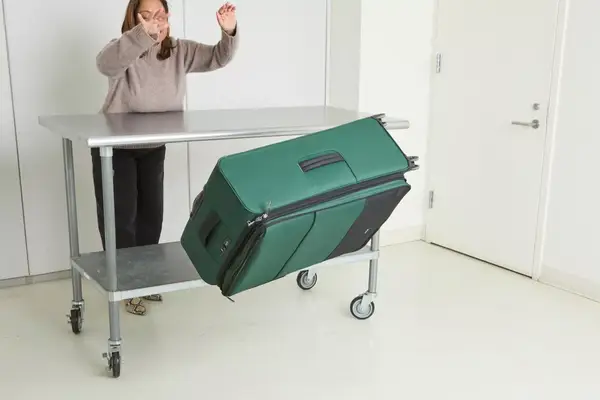 A person throws the Antler Soft Stripe Lightest Large Luggage off of a wheeled cart